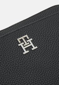 Musta tekstuuri nahkapinta, jossa on hopeinen metallietiketti, jossa on sotkeutuneet kirjaimet "T" ja "H."