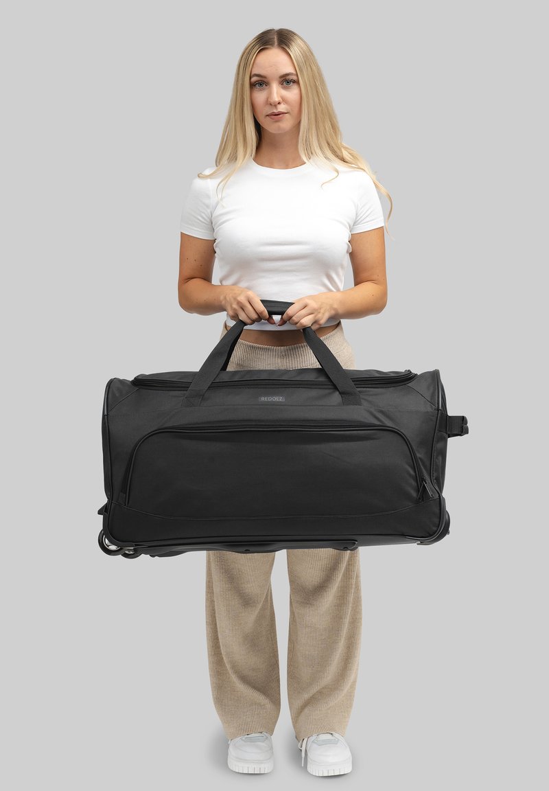 Sac de sport noir en tissu résistant, doté de poignées doubles, d'un compartiment principal zippé et d'une surface lisse sans motifs visibles.