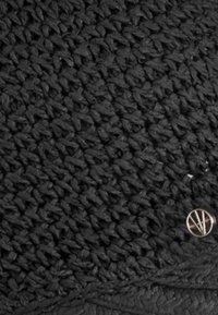 Tela negra tejida con una superficie texturizada, que presenta un acento de logo metálico redondo. El diseño muestra un primer plano del patrón entrelazado del material.