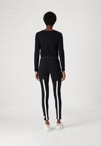 Zwarte long-sleeve top en zwarte leggings met witte zijstrepen, heeft een slim fit en elastische tailleband, gecombineerd met witte sneakers.