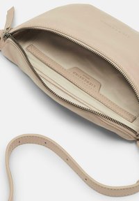 Bolso de cuero beige con cierre de cremallera, interior forrado de tela y correa desmontable. Presenta un logotipo en relieve y una textura suave.