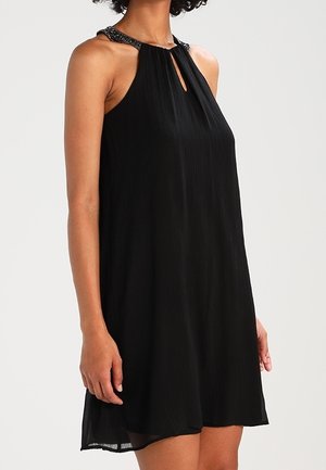 Sleeveless black dress with a beaded halter neckline and a small keyhole cutout at the chest, worn mid-thigh length.