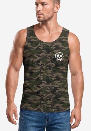 Man wearing sleeveless camouflage tank top with a small white skull graphic on the chest and blue jeans, looking to the side.