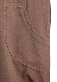 Close-up of a brown fabric garment showing a large, curved front pocket with detailed stitching and textured material.