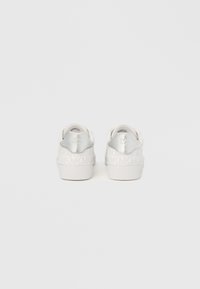 Baskets blanches avec un motif texturé du logo MK, des accents argentés lisses au talon et une semelle en caoutchouc propre. Vue arrière.