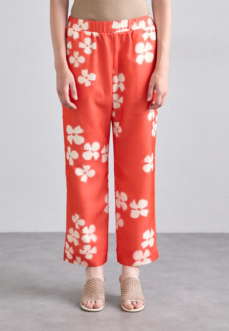 Red floral-patterned pants with an elastic waistband, featuring large white flowers. Texture appears smooth; wide, cropped legs.