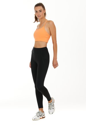 Orange sportbehå, svarta högmidjade leggings och silverfärgade träningsskor med orangea detaljer. Slätt material och åtsittande design för aktiv klädsel.