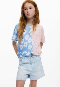 Pamut póló, osztott dizájnnal: bal oldalon kék színű, fehér margarétákkal, jobb oldalon rózsaszín szív mintával; világos farmer rövidnadrággal párosítva.