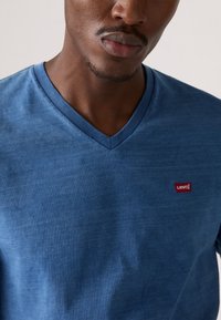 Kék pamut V nyakú póló, bal mellen egy kis piros Levi's logóval. Az anyag kissé texturált hatású.
