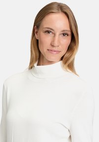 Fehér garbó pulóver ribbed nyakkal és hosszú ujjakkal, sima, puha anyagból készült, testhezálló kialakítással és varrás nélküli vállrésszel.