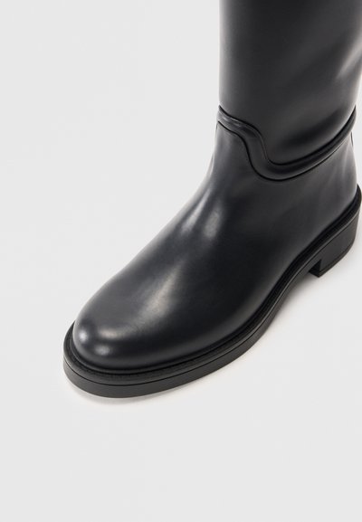 Bota de cuero negro hasta la rodilla con superficie lisa, puntera redondeada, tacón bajo y detalle de costura sutil en el tobillo.