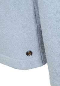 Lichtblauwe gestructureerde sweater van een zachte stof. Heeft een zwart hexagonaal logo met gele strepen bij de zoom. Gebogen onderste rand.