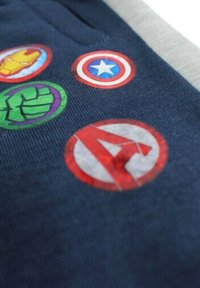 Un tissu bleu foncé présente divers écussons colorés avec les logos de super-héros : Iron Man, Captain America, Hulk et les symboles des Avengers en détails vibrants.