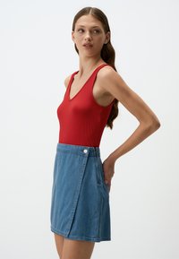Body rosso a coste con scollatura a V, abbinato a una gonna A-line in denim con zip laterale e chiusura a bottone.