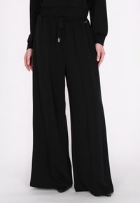 Zwarte wijde broek gemaakt van zachte stof, met een elastische tailleband en trekkoord, en accenten van zilverkleurig beslag.