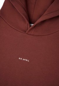 Burgundi színű kapucnis pulóver, puha anyagból készült. Középen fehér "OH APRIL" felirat található, valamint klasszikus kapucni dizájn jellemzi.