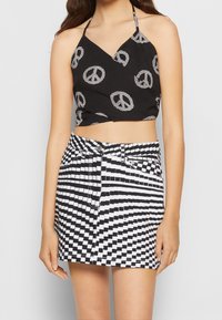 Černý crop top se vzorem bílého symbolu míru; spárovaný s černobílou kostkovanou mini sukni s mašlí v pase.