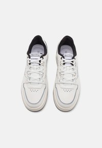 Hvide sneakers med en glat læderoverdel, sort indvendig foring, grå detaljer og perforerede områder på tåen. Renset design med snørebånd.