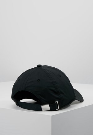 Casquette de baseball noire posée sur une surface blanche, montrant une sangle ajustable avec une boucle métallique à l'arrière.