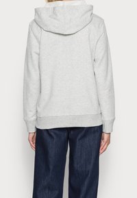 Sweat à capuche gris avec cordon de serrage, poignets et ourlet côtelés ; associé à un jean large bleu foncé. Texture du tissu lisse, sans motifs visibles.