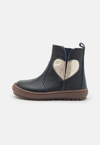 Bottine en cuir noir avec un accent cœur doré, semelle en caoutchouc marron et panneaux latéraux élastiques pour un enfilage facile. Surface texturée.
