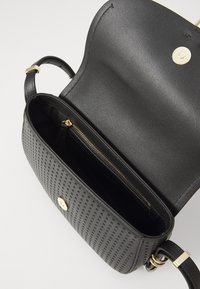 Borsa a tracolla in pelle nera con texture perforata, hardware dorato e tasca interna con zip. Caratterizzata da una tracolla e chiusura a scatto.