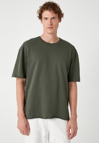 Olivengrøn kortærmet t-shirt med rund halsudskæring, afslappet pasform og råkanter på ærmerne, lavet af blødt bomuldsstof.