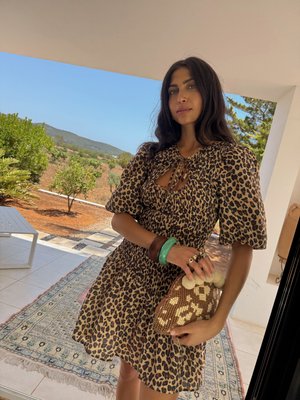 Leopardprint jurk met pofmouwen en een keyhole halslijn, gecombineerd met een gestructureerde, bruin en crèmekleurige gehaakte handtas. Groene en bruine armbanden.
