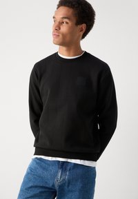 Hanorac negru cu un design cu panouri texturate, guler rotund și manșete ribbed. Purtați peste o cămașă albă, asortat cu blugi albaștri.
