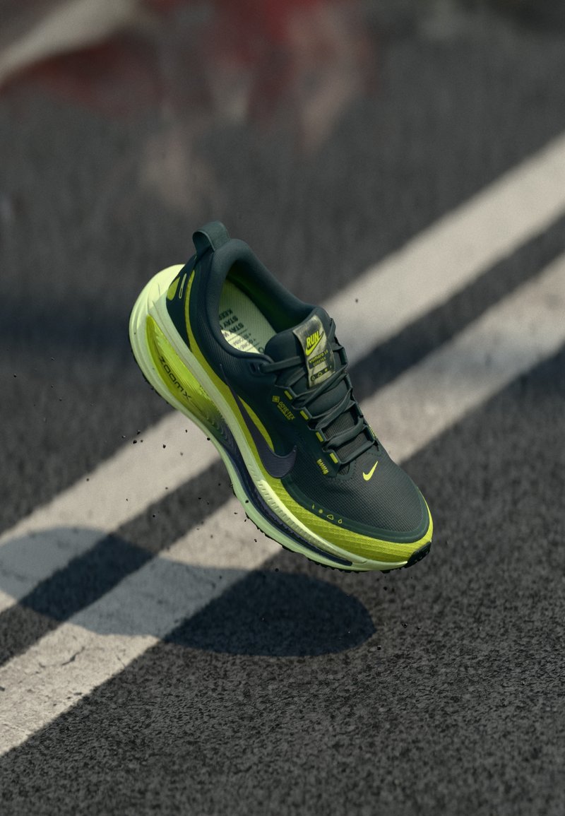 Green and yellow athletic shoe, featuring a textured upper, lightweight design, and cushioned sole, shown airborne above a street.