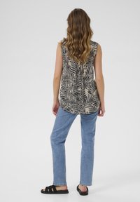 Ærmeløs beige top med sort bladmønster, båret med lyseblå jeans og sorte sandaler. Toppen har en buet kant og en afslappet pasform.
