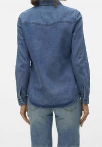 Denim shirt in dark blue, long sleeves, pointed collar, back yoke detail, and buttoned cuffs. Tapered fit with rounded hem.