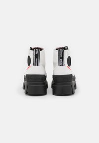 Botines blancos con un diseño de tobillo alto, suela negra en contraste, acentos de marca en negro y un acabado texturizado en el material superior.