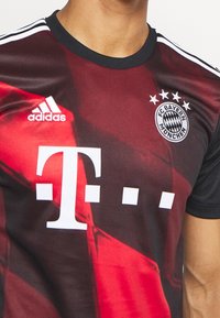 Maglietta sportiva rossa e nera, a maniche corte, con colletto nero. Presenta il logo Adidas, il badge del FC Bayern Monaco e testo bianco dello sponsor.