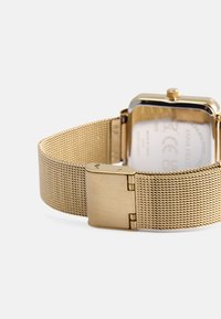 Ρολόι με χρυσό πλέγμα από λουράκι που διαθέτει ορθογώνια κάσα, ατσάλινη πλάτη και ασφαλές κούμπωμα. Λείο υλικό με γυαλιστερή φινίρισμα.