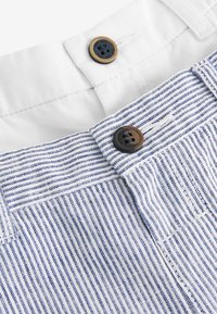Blue and white striped fabric with two buttons; one is dark brown and rounded, the other is black with a textured surface. Cotton material.