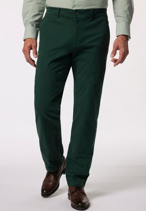 Homme portant un pantalon droit vert foncé, des chaussures habillées en cuir marron et une chemise à rayures vert clair avec boutons.