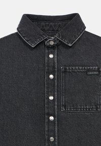 Μαύρο τζιν πουκάμισο με κλασικό γιακά, ασημένια κουμπιά snap και θηκούλα στήθους με ετικέτα Calvin Klein. Υφή υφάσματος, ίσια γραμμή.