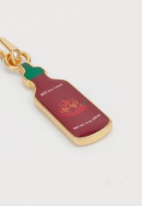 Bouteille de sauce chili rouge en charme avec un capuchon vert, des accents dorés et une étiquette imprimée présentant des graphiques de flammes et de piments. Contient 9 oz (255 g).