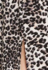 Tessuto stampa leopardato che presenta una combinazione di tonalità nere, grigie e beige con un dettaglio di spacco laterale, che mette in mostra una superficie tessuta e strutturata.