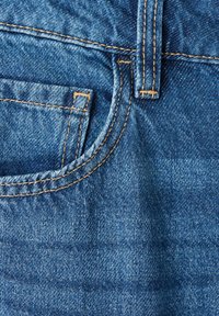 Gros plan d'une poche de jean denim bleu avec couture jaune et partie d'une boucle de ceinture.