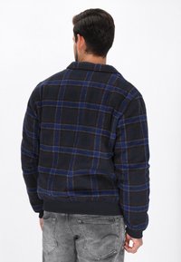 Schwarze und marineblaue Karofleecejacke mit einem Kragen und elastischen Bündchen. Verfügt über kontrastierende blaue und rote Linien, die für Wärme und Komfort sorgen.