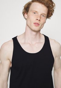 Débardeur noir en coton, doté de larges bretelles, d'un col rond et d'une texture lisse. Le tissu semble doux et flexible.