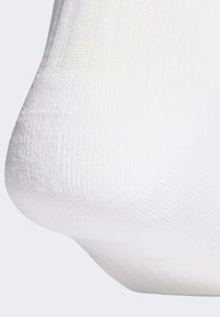 Bílá ponožka s žebrovanou strukturou, hladkým povrchem a polstrovanou patou. Materiál vypadá lehký a pružný, vhodný pro pohodlí.