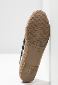 Semelle d'une chaussure espadrille taille 37 avec côtés tissés et dessus en tissu à carreaux noir et blanc reposant sur une surface blanche.
