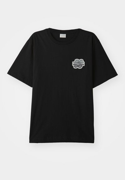 T-shirt noir en coton avec un col rond et des manches courtes. Présente un patch floral gris sur la poitrine gauche. Design simple et sans embellissements.