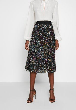 Blouse blanche à manches longues avec encolure fendue, associée à une jupe midi noire plissée ornée d'un imprimé abstrait coloré de confettis. Escarpins noirs.