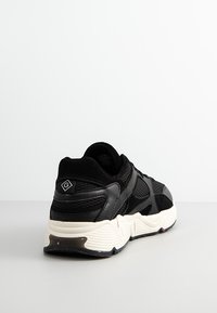 Schwarze Sneaker mit Obermaterial aus Mesh und Synthetik, dicker weißer Sohle, strukturierten Details und Logo-Patch an der Ferse.