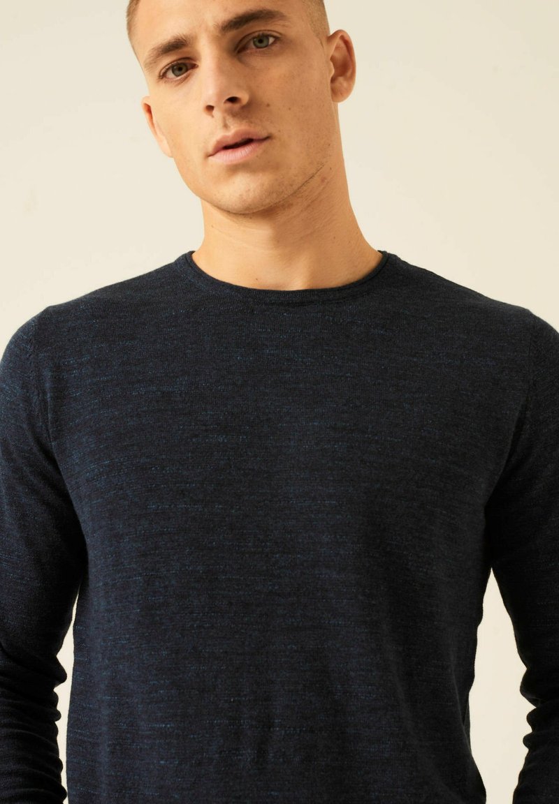 Dunkelblaues Langarmstrickshirt mit einem runden Ausschnitt, das aus einem strukturierten Stoff besteht und dezente hellblaue Flecken enthält.