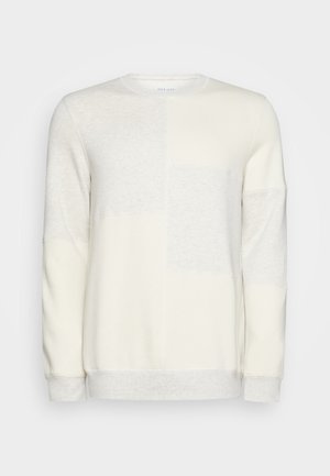 Sudadera beige claro con cuello redondo, que presenta un diseño de patchwork con diferentes texturas y tonos de crema. Puños y dobladillo acanalados.